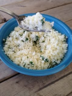 a blue bowl filled with rice and spinach on top of a wooden table next to a spoon