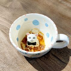 a cat figurine sitting in a cup filled with honeys and syrup on top of a wooden table