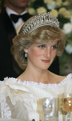 the princess is wearing a tiara and sitting at a table with wine glasses in front of her