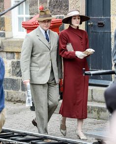 the man and woman are walking down the street together, dressed in old fashion clothing