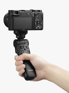 a hand holding a small camera on top of a tripod in front of a white background