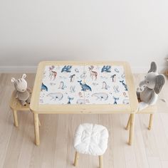 two stuffed animals sitting on stools next to a wooden table with a white blanket