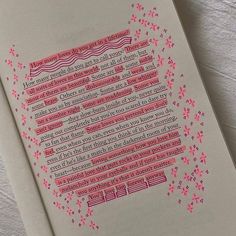 an open book with pink and red writing on the page next to a cup of coffee