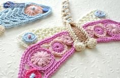 three crocheted necklaces are laying on a white tablecloth, one is pink and the other is blue