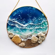 a blue and white plate with some rocks on the beach in front of it that is hanging from a gold chain