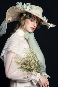 a woman in a white dress and hat with flowers on her head is holding a bouquet