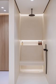 an empty bathroom with white walls and lights on the ceiling, along with a black shower head