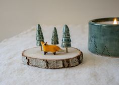 a small yellow fox figurine sitting on top of a piece of wood next to a candle