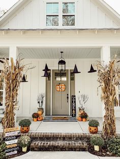 a white house decorated for halloween with pumpkins and corn stalks on the front porch