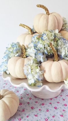 a white bowl filled with flowers and pumpkins on top of a blue table cloth