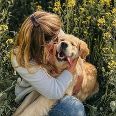 a woman sitting in the grass with her dog and holding it up to her face