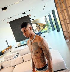 a man standing in front of a couch with tattoos on his chest and arms, looking down