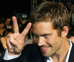 a man is making the peace sign with his hand while standing in front of a crowd