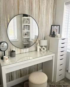 a white desk with a round mirror on it's wall and drawers underneath the table