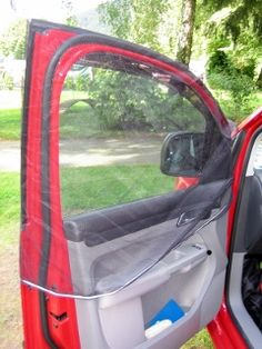 the side view mirror of a red truck parked in front of a tree and grass area