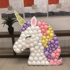 a unicorn made out of balloons sitting on top of a table next to a potted plant