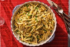 a bowl filled with pasta on top of a red table cloth next to silverware