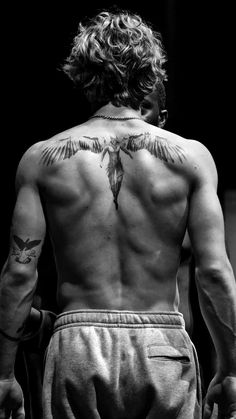 the back of a man with tattoos on his upper and lower body, looking down