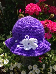 a purple crocheted hat with white flowers in the background