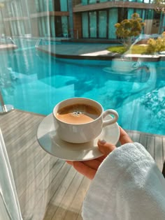 a person holding a cup of coffee on top of a saucer next to a swimming pool