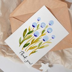 a thank you card with watercolor flowers on it next to an envelope and cross