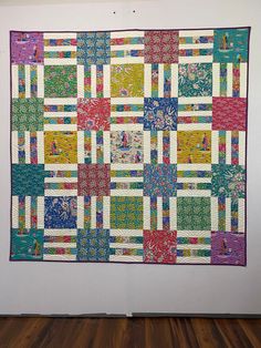 a colorful quilt hanging on the wall next to a wooden floor