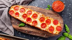 a pepperoni pizza on a wooden cutting board next to some sauce and basil leaves