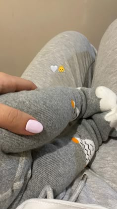 a woman with pink nails is laying on her stomach wearing grey sweatpants and white heart stickers