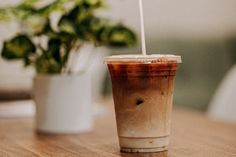 a drink sitting on top of a wooden table next to a potted green plant