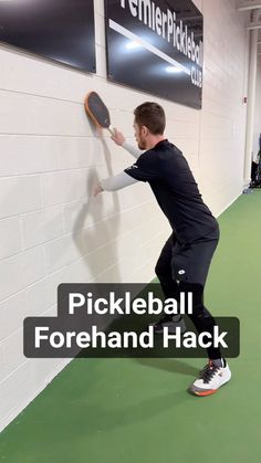 a man holding a tennis racquet on top of a green floor next to a wall