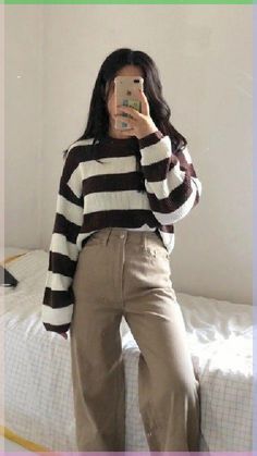 a woman is taking a selfie in her bedroom while wearing brown pants and a striped sweater