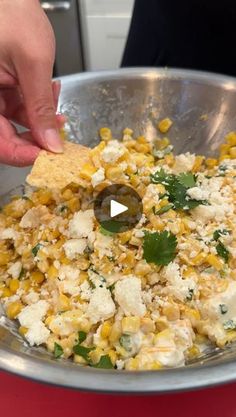 someone is dipping some tortilla chips into a bowl filled with corn and cheese