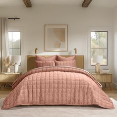 a bed in a bedroom with pink comforter and pillows on the floor next to two nightstands