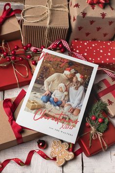 a christmas card surrounded by presents and other holiday items on a wooden table with red ribbon