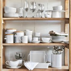 a wooden shelf filled with white dishes and silverware on top of eachother