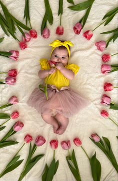 a baby girl in a tutu skirt surrounded by pink flowers and tulips