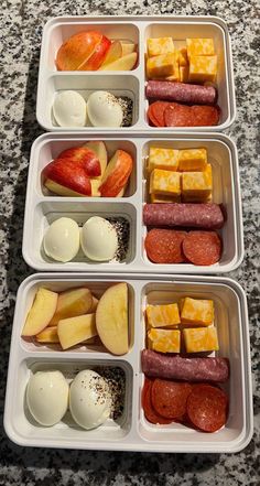 four plastic containers filled with food on top of a granite countertop next to an apple, cheese, and sausage