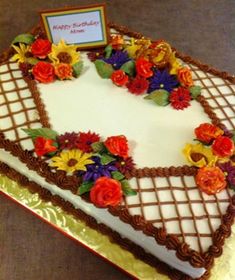 a heart shaped birthday cake with flowers on the top and bottom, sitting on a table