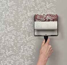 a person using a paint roller to paint a wall with white flowers on the background