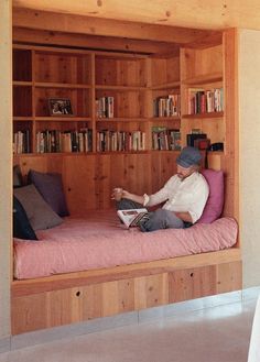 a man sitting on top of a bed in a bedroom next to a book shelf