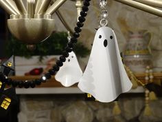 two white ghost ornaments hanging from a chandelier with black beads and gold accents