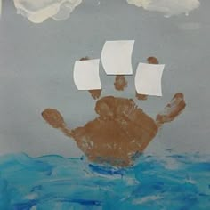 a child's hand is in the water with two white paper ships floating above it