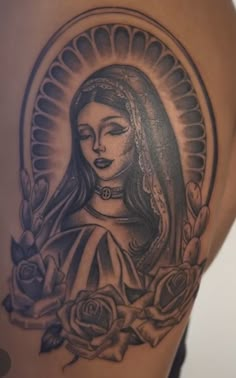 a woman's tattoo with roses and a virgin mary in the center on her thigh