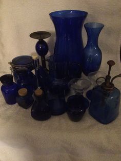 a collection of blue glass vases sitting on top of a white cloth covered floor