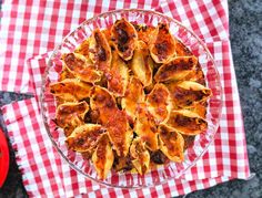 a glass bowl filled with pasta on top of a red and white checkered table cloth