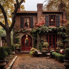 an old brick house with red doors and shutters on the windows is surrounded by greenery