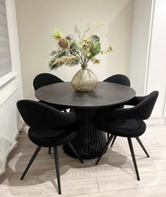 a round table with black chairs around it and a vase filled with flowers on top