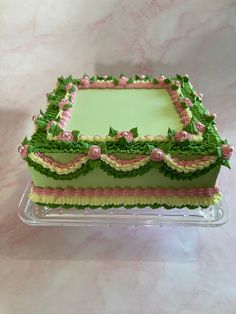 a cake with green and pink decorations on top of a glass platter that is sitting on a table