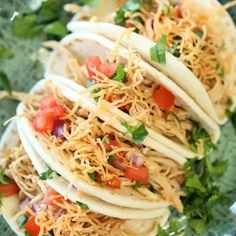 three tacos with shredded cheese, tomatoes and cilantro on a green plate