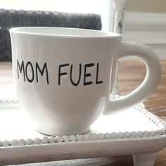 a white coffee cup with the word mom fuel written on it sitting on a table